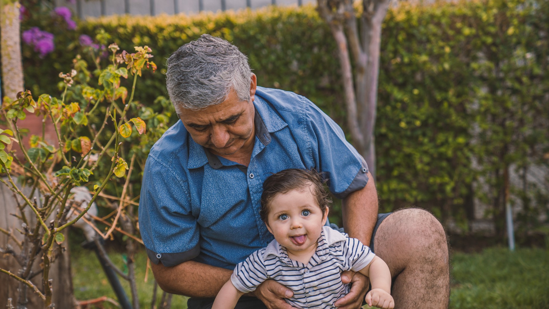 Grandfather wearing a blue shirt hold his grandchild making a silly face