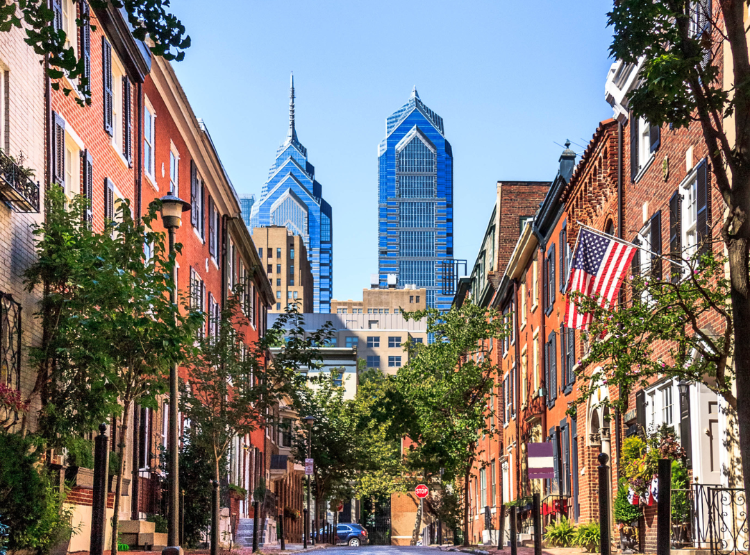 the skyline of philadelphia as seen through a street of rowhomes