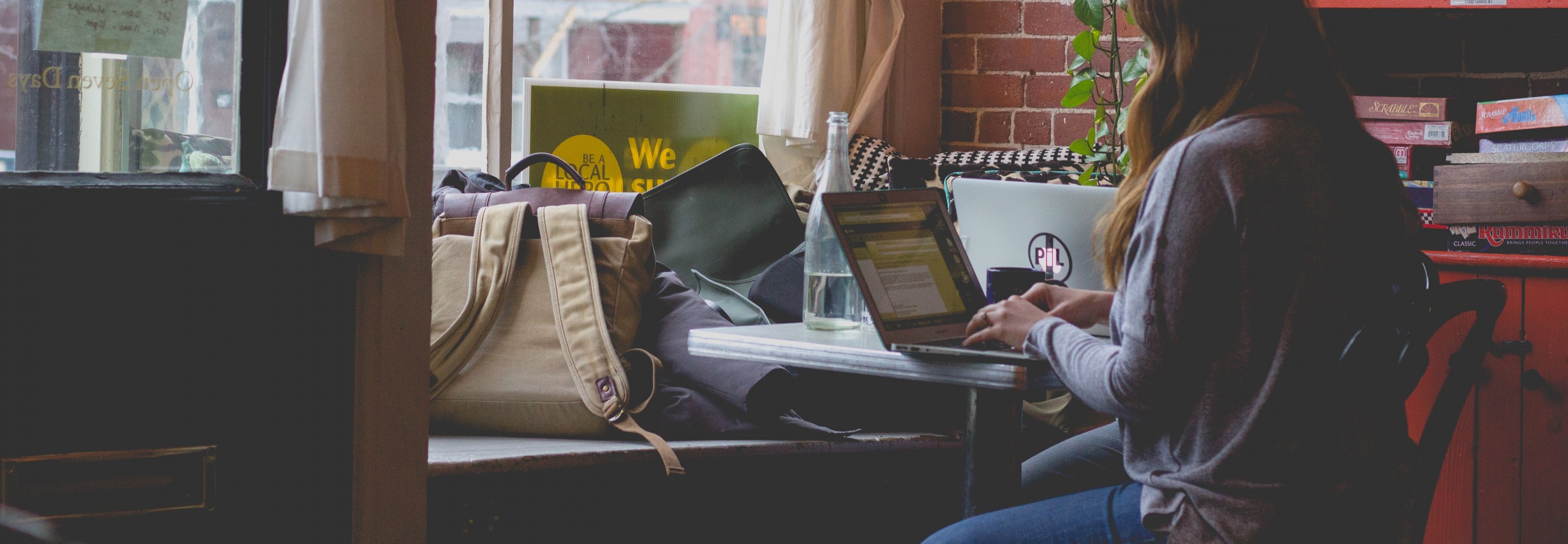 Photo of woman typing on a computer. She sits at a desk in front of a bright window in a cozy room.Photo by Bonnie Kittle on Unsplash