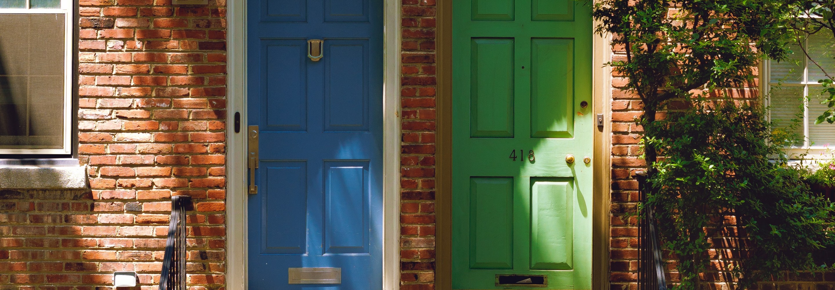 Photo of two rowhomes. One door is painted bright green and one is painted bright blue.  Photo by Tyler Finck on Unsplash