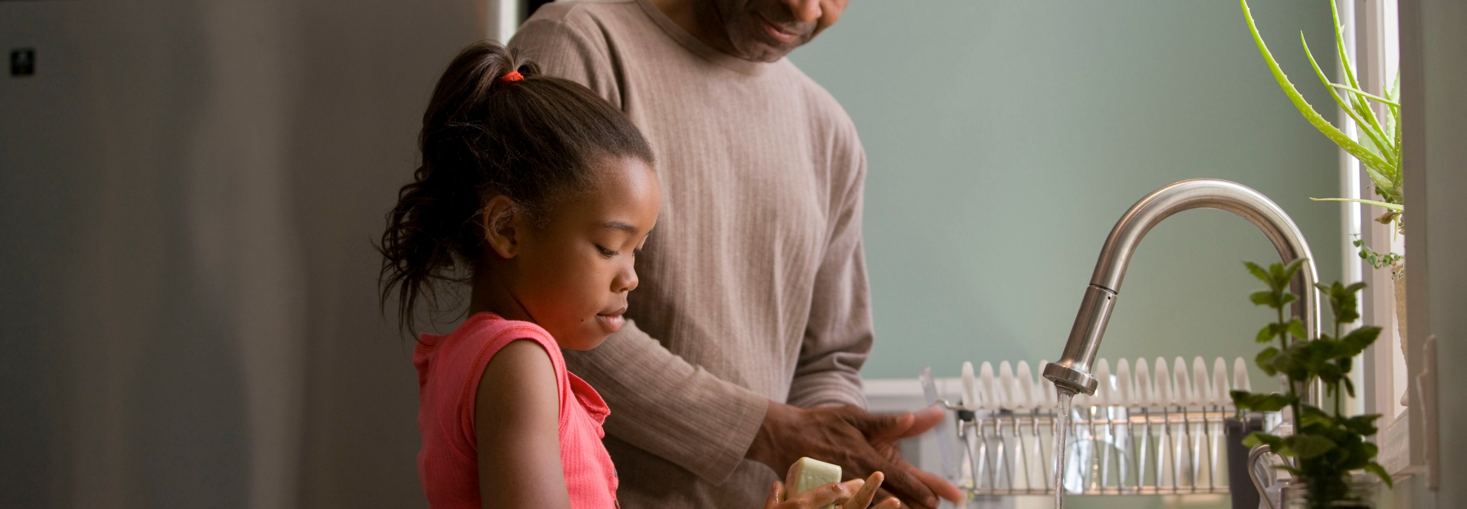 An adult and child washing their hands in the kitchen; Photo by CDC on Unsplash