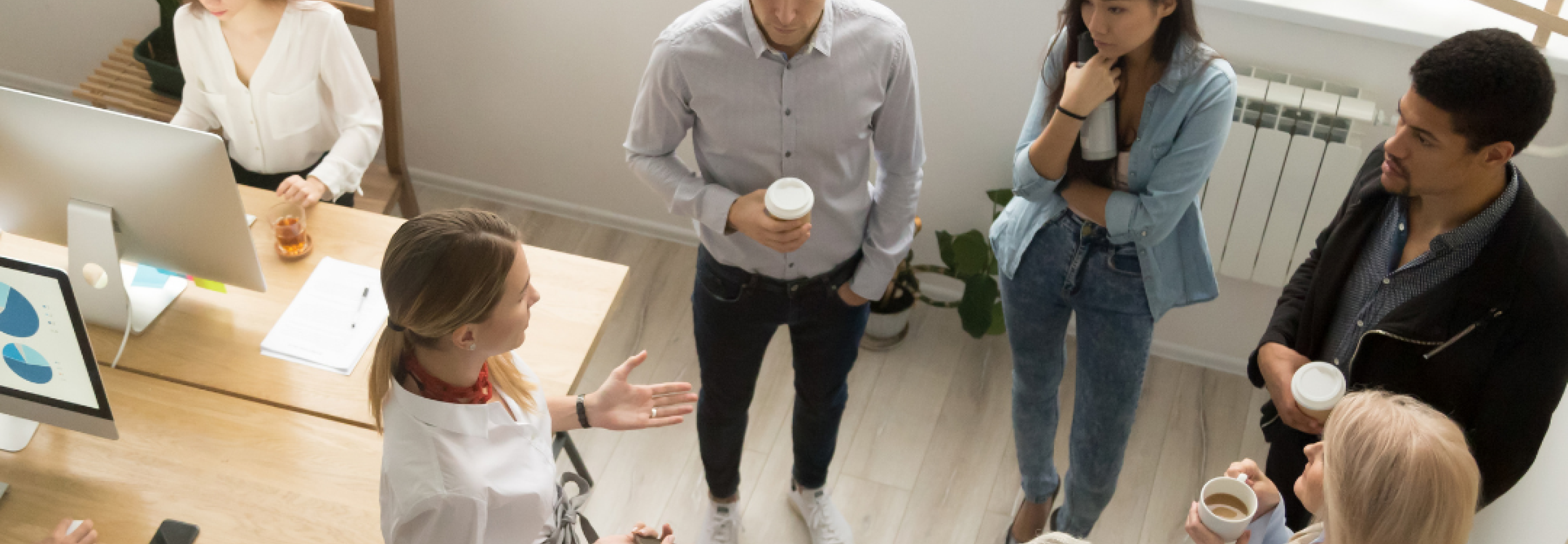 A group of young professionals stands in a circle in an office chatting