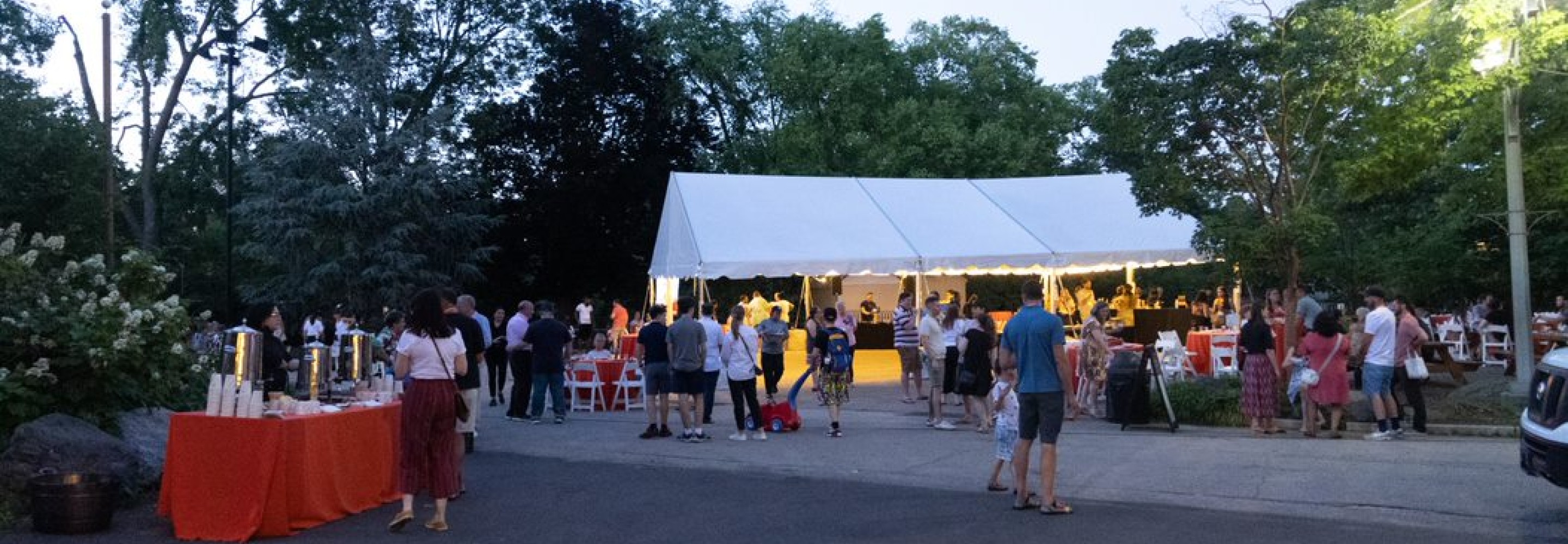 Party goers socialize in and around a large white tent underneath trees at the Zoo