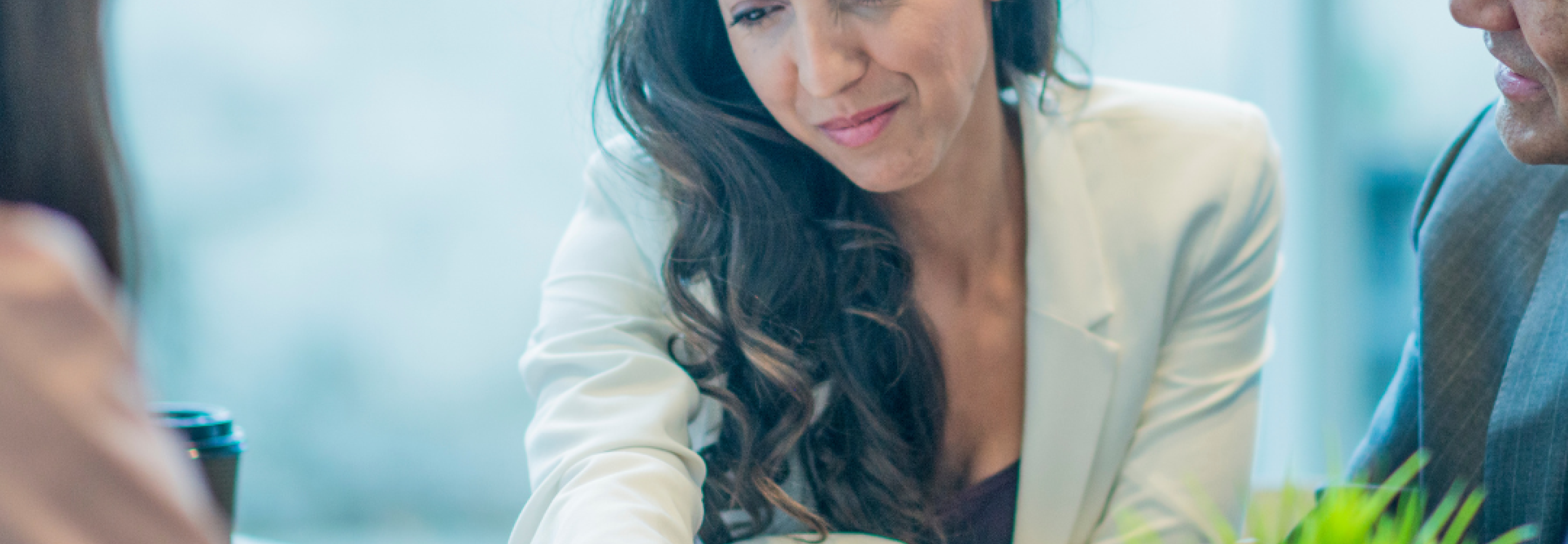 A woman in a white business suit looks over paperwork in a room full of people