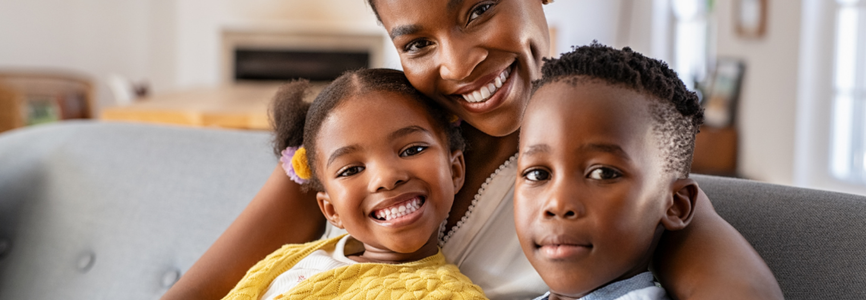 A mother and her two children sit on the couch and smile at the camera