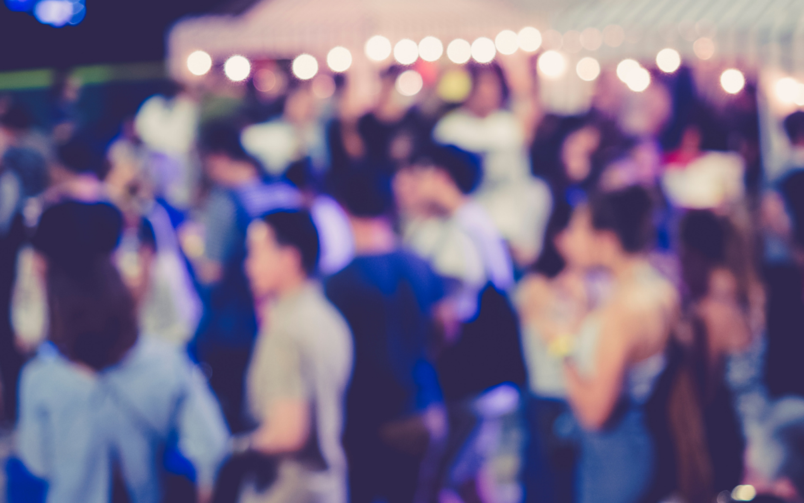 blurry crowd of event goers hangs out under string lights