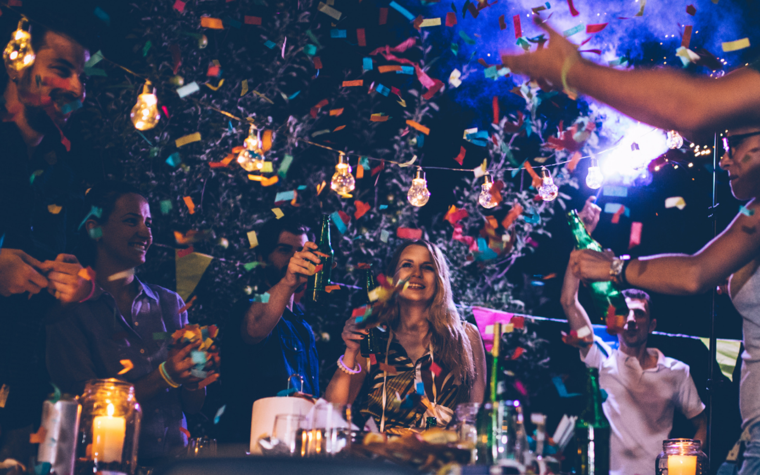 A group of people throws confetti around a table of food and drinks