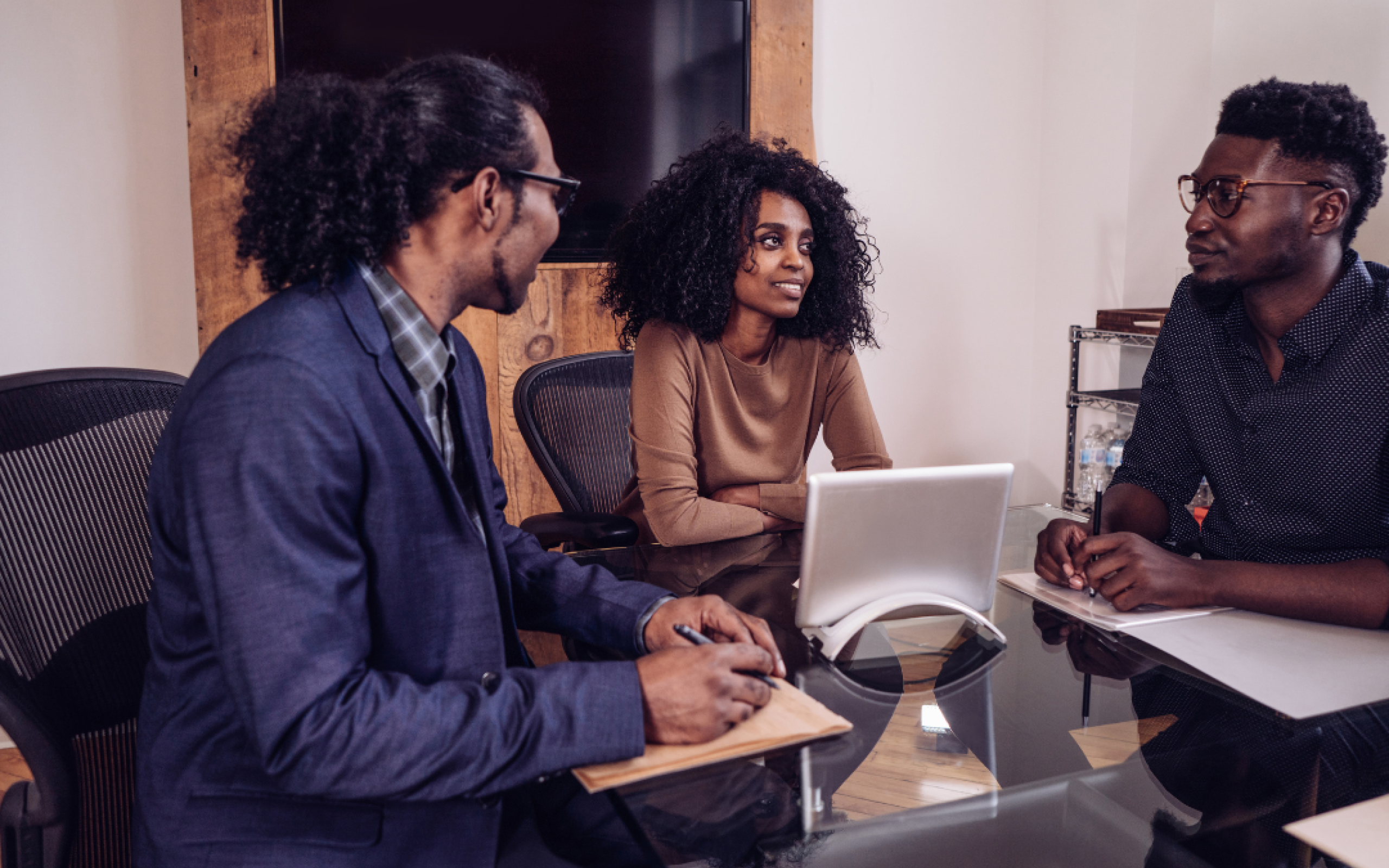 Three young professionals sit around a table and a tablet