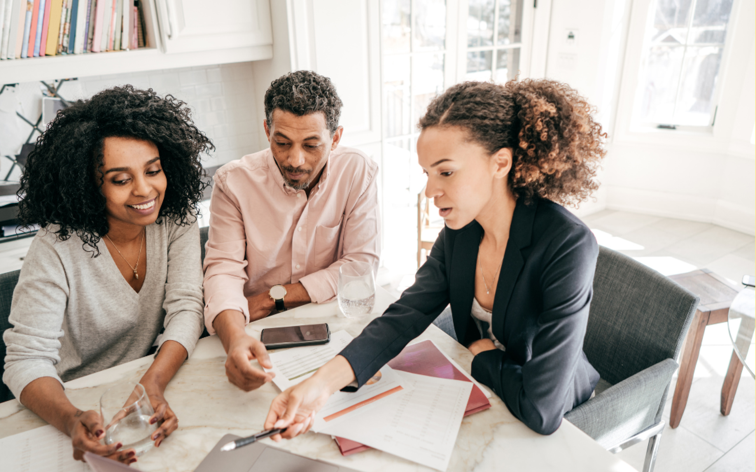 A man and a woman consult with another woman over paperwork and a computer.