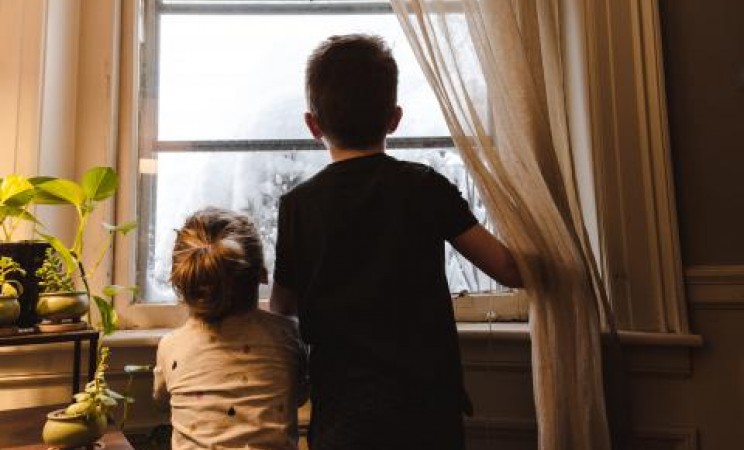 Two young brothers looking out the window of their home
