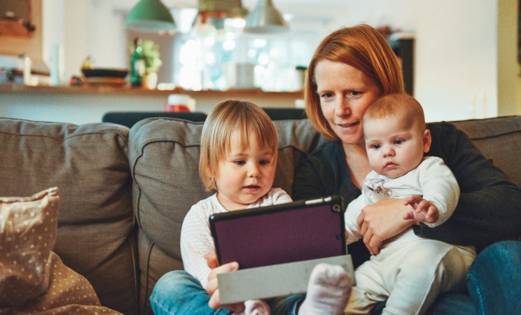 Woman holds infant in her left arm and toddler in right. Photo by Alexander Drummer on UnSplash.