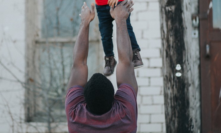 an adult man plays a game with his son, tossing him into the air