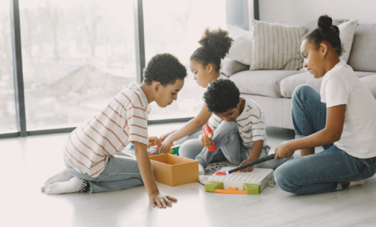 Four children sit on the floor of a modern apartment playing with toys.