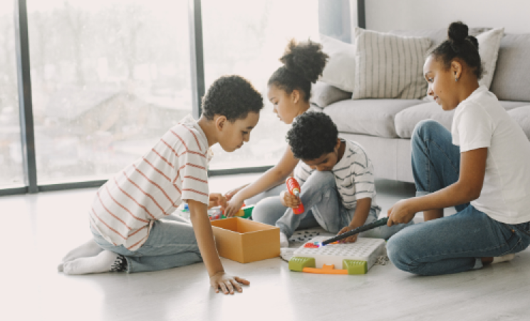 Four children sit on the floor of a modern apartment playing with toys. 