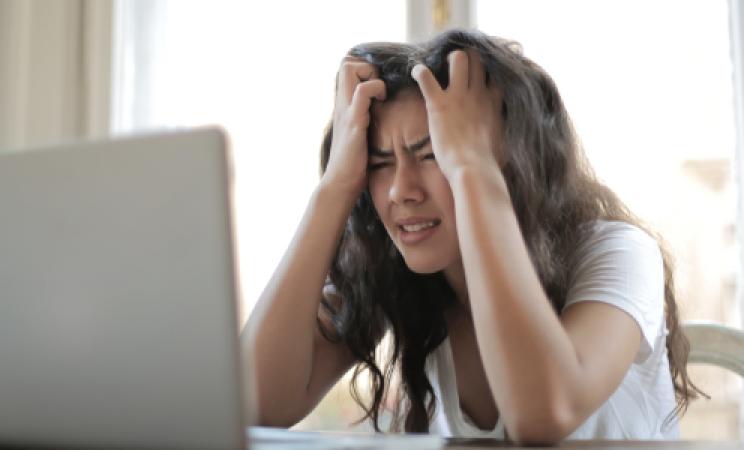 A young woman sits at a desk in front of a computer pulling on her fair in frustration