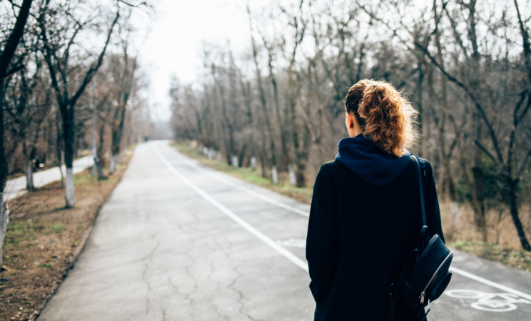 A woman stares down a long and empty road