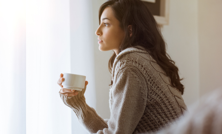 A woman sits pensively with a cup of tea in her hand
