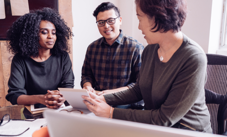 two people sit in an office with a third person who is a tax preparer looking over their tax information