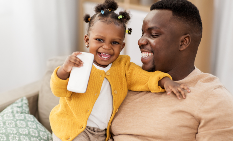 A father holds his toddler daughter who is smiling at the camera