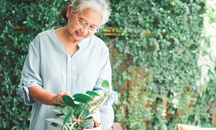 An older woman tends to a potted plant with a smile on her face