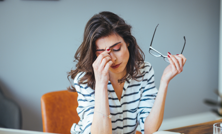 A stressed woman rubs her temples while looking over bills. 