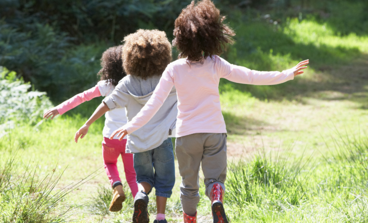 Three children walk along a path in nature with rainboots on