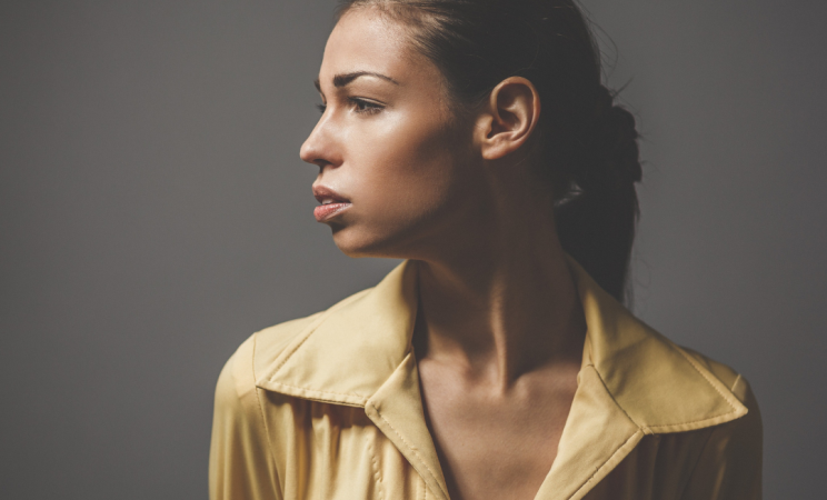 a woman in a tan blouse looks sadly to the side