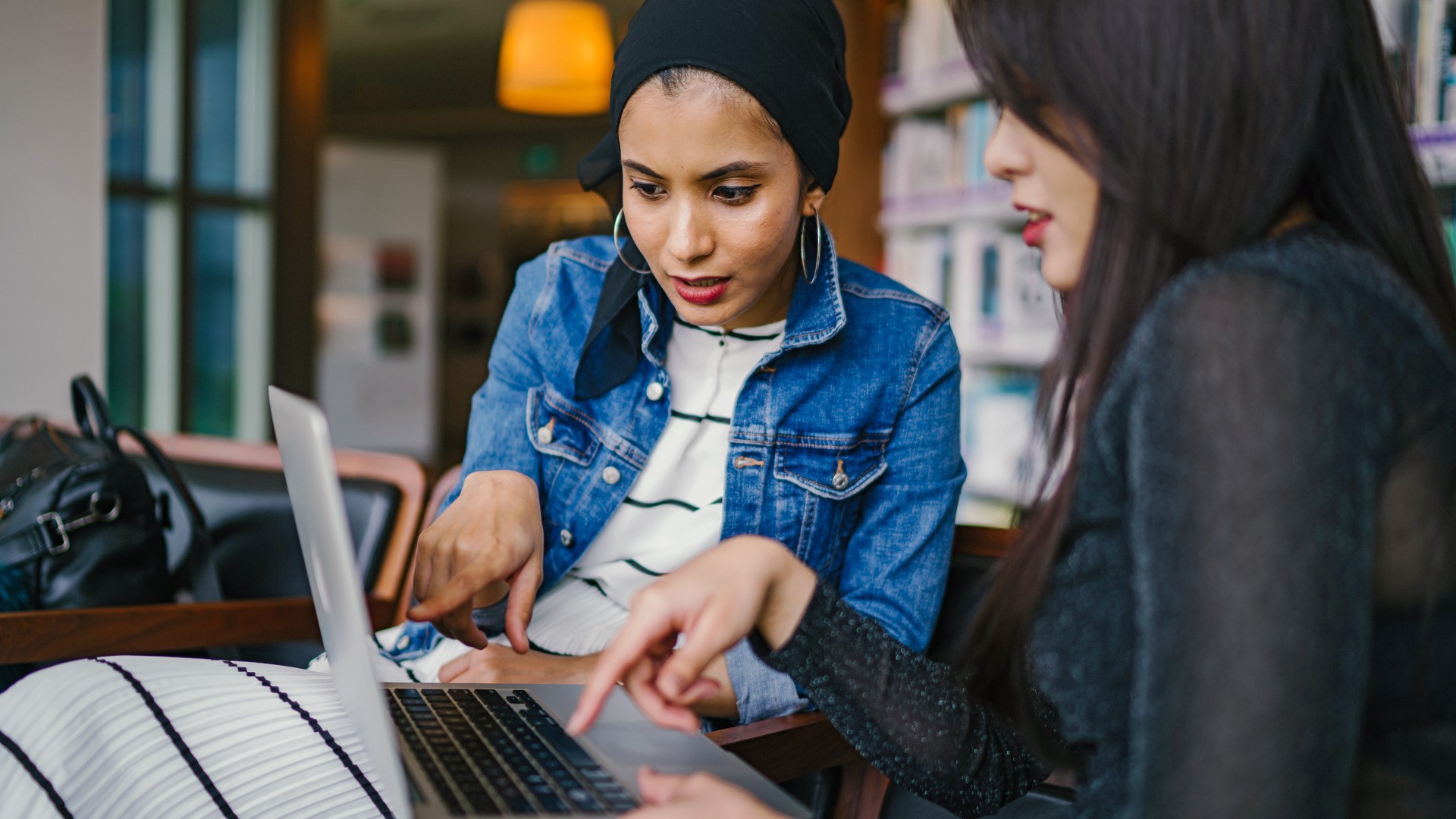 Two women-presenting individuals look at a laptop in an office setting