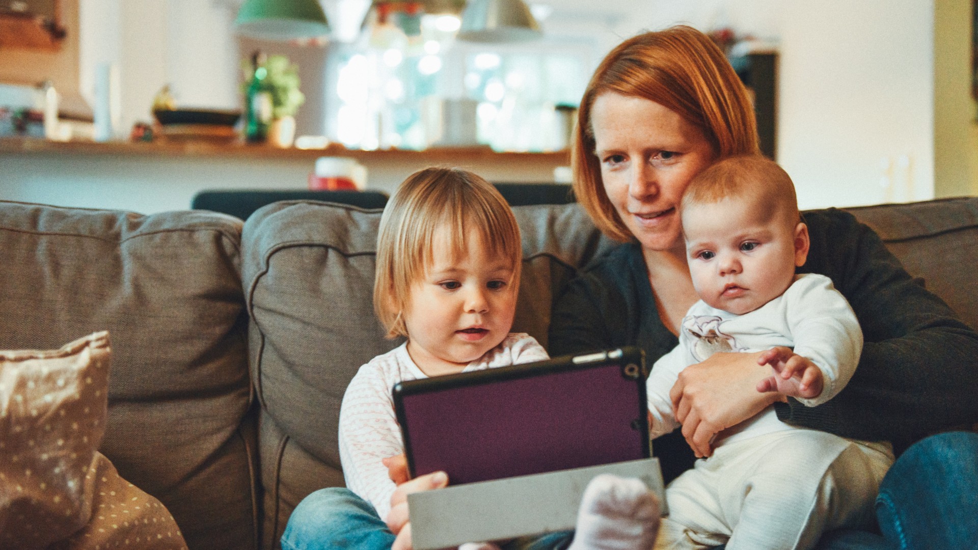 Single mother holds toddler in right arm and infant in left. Photo by Alexander Drummer on UnSplash.