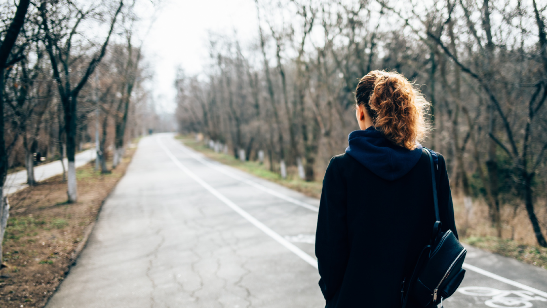 A woman stares down a long an empty road