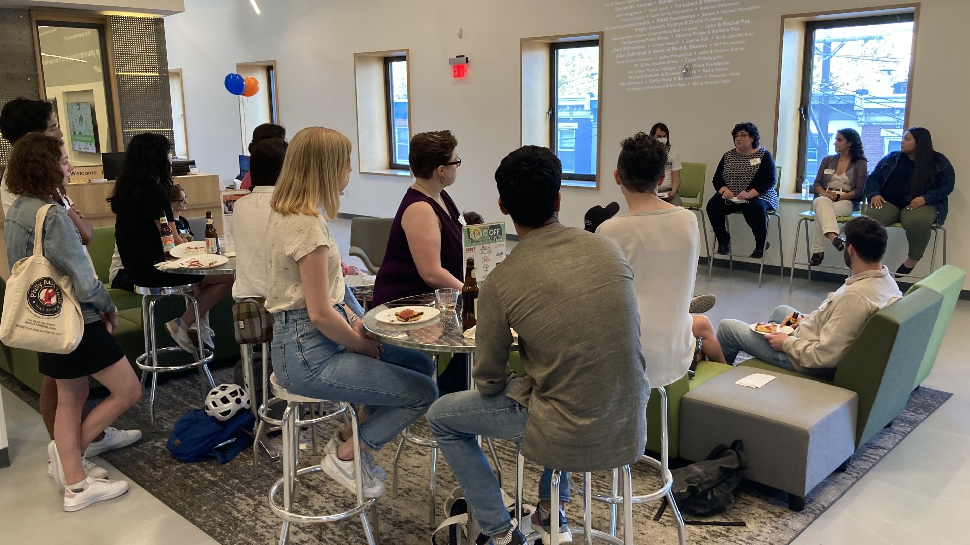 People sit in the lobby of MANNA watching a four person panel