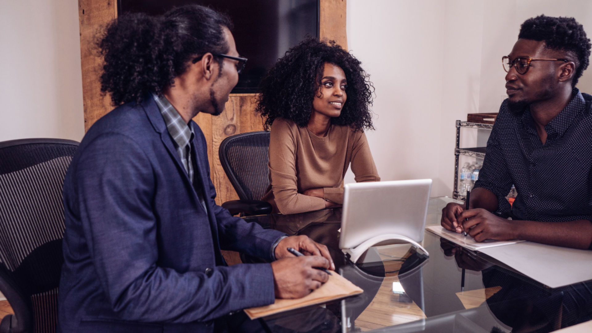 Three young professionals sit around a table and a tablet