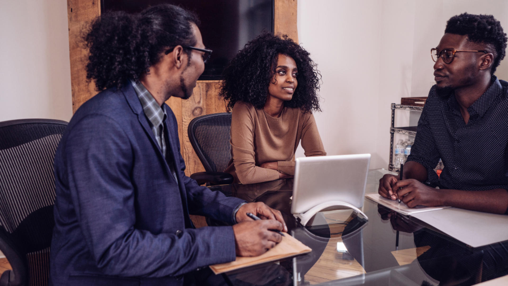 Three young professionals sit around a table and a tablet 