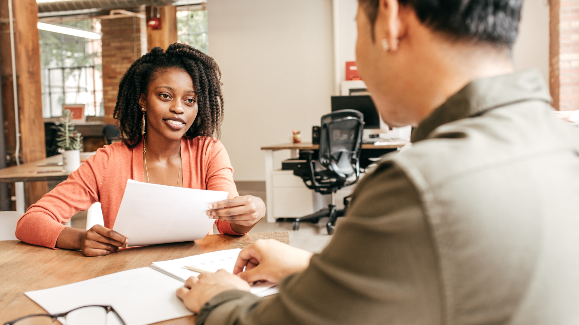 A woman interviews a man for a job. She is holding his resume in her hand.