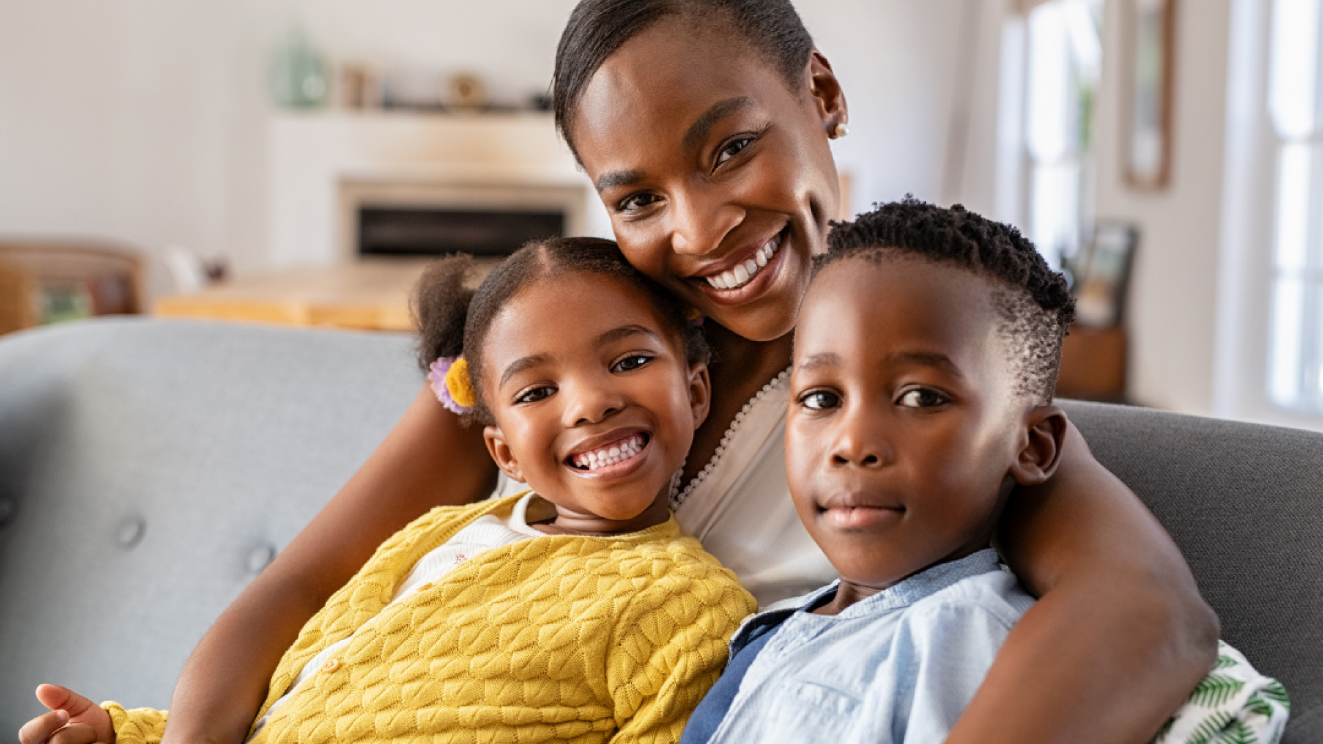 A mother and her two children sit on the couch and smile at the camera