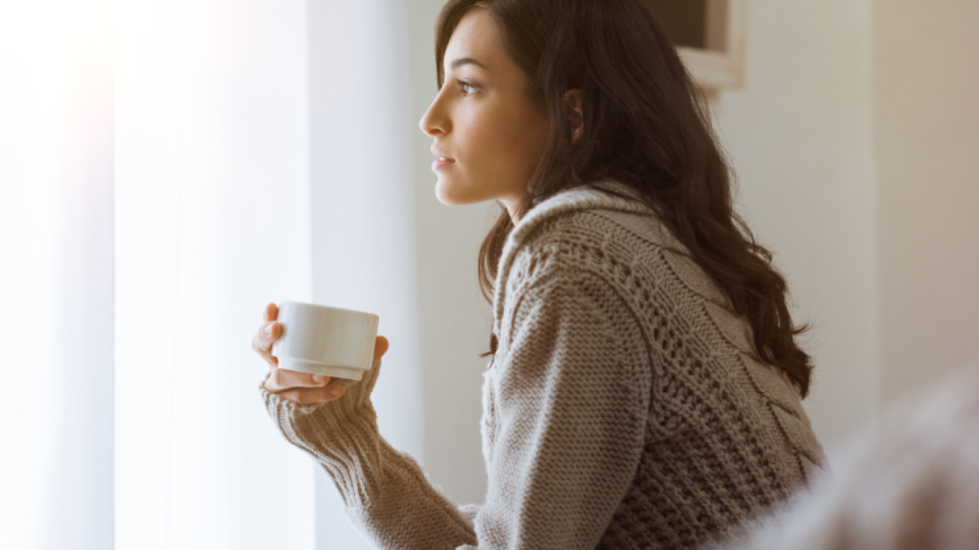 a woman with a cup of tea in her hand looks out the window