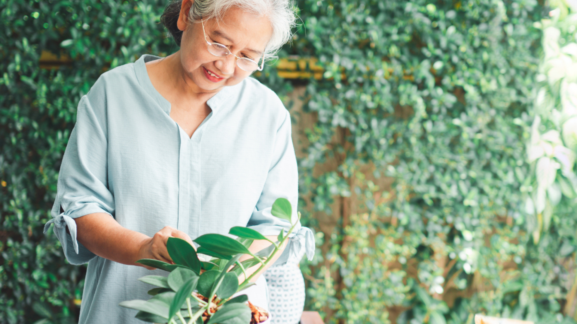 An older woman tends to a plant in a pot