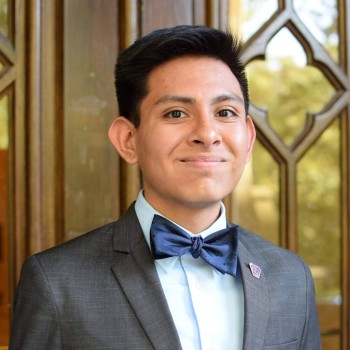 Luis Bravo poses in a suit and bowtie in front of glass doors.