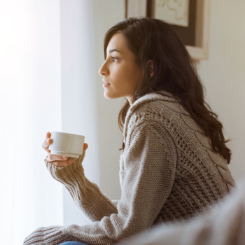 A woman sits pensively with a cup of tea in her hand