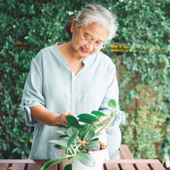 An older woman tends to a potted plant with a smile on her face