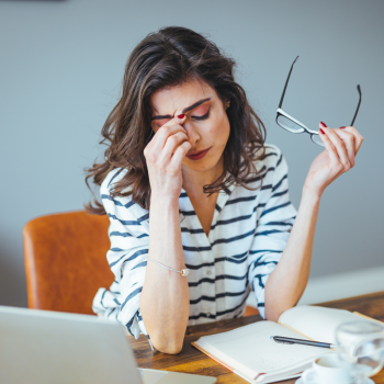 A stressed woman rubs her temples while looking over bills. 