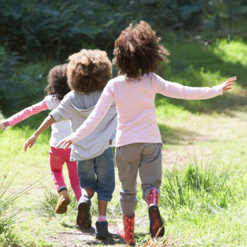 Three children walk along a path in nature with rainboots on