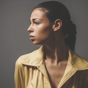 a woman in a tan blouse looks sadly to the side