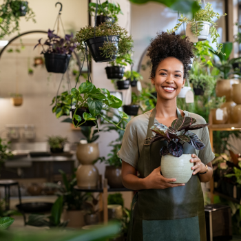 A woman who owns a plant store poses for a photo holding a plant 